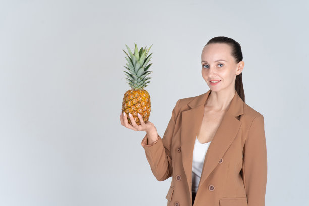 身着米色西装的微笑女子。手里拿着一个成熟的蜜汁菠萝。横幅,复制空间。图片下载