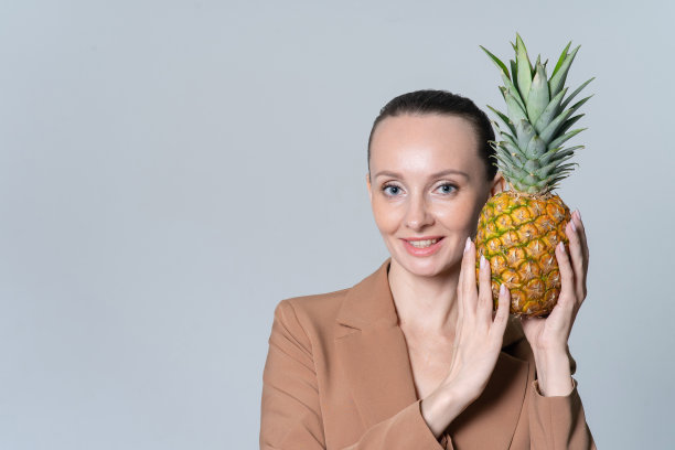 穿着商务米色夹克的微笑快乐的女人。手里拿着一个成熟多汁的菠萝。健康饮食食品的概念。图片下载