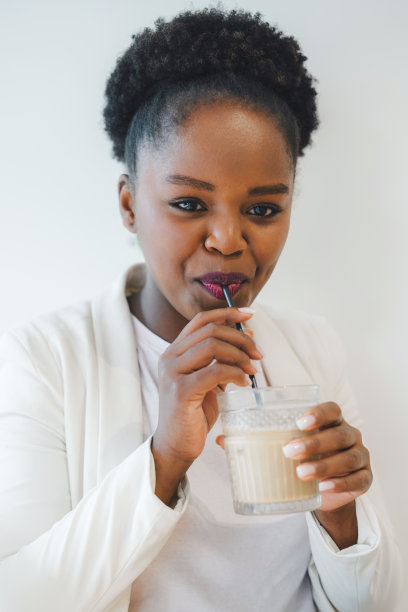 画像一个微笑的黑人年轻女子在咖啡店放松，喝拿铁咖啡。美丽的年轻女子正在享受拿铁。特写女孩喝拿铁咖啡的脸。图片下载