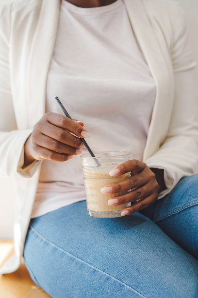 黑色的女性手拿冷饮的杯子坐在咖啡店里。人们的生活方式。现代的生活方式。图片下载