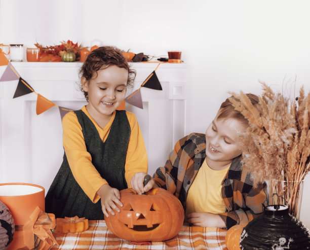 年轻的孩子，女孩和男孩雕刻传统的万圣节南瓜灯与恐怖的面孔在家里聚会图片下载