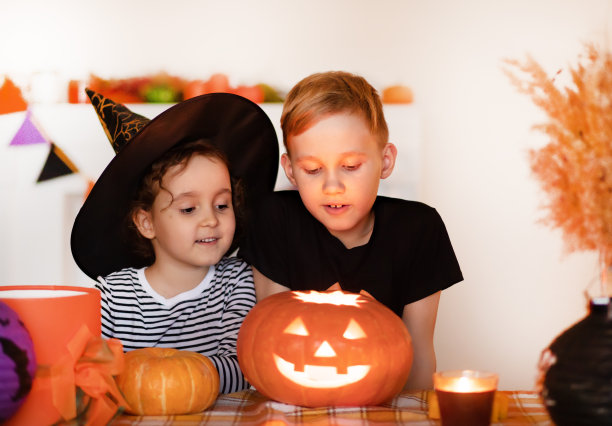 年轻的孩子，女孩和男孩雕刻传统的万圣节南瓜灯与恐怖的面孔在家里聚会图片下载