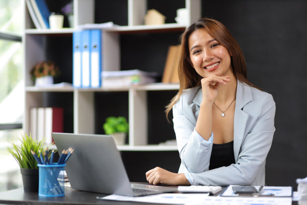 一个迷人的商业女性的肖像快乐在她的办公桌在办公室。图片下载