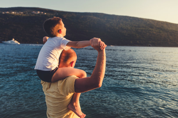 父亲和儿子在日落海滩上。爸爸和儿子在夏日的沙滩上一起玩耍。图片下载