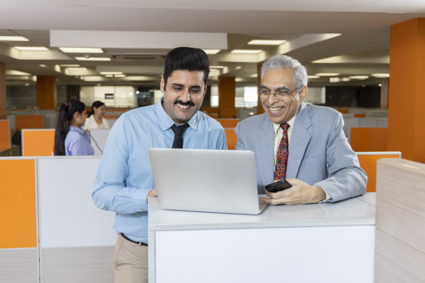 快乐成熟的商人和他年轻的助手在办公室工作。图片下载