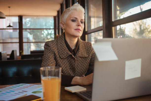 50岁的资深女性，美丽而时尚，坐在咖啡馆，用笔记本电脑工作，自由设计师。看起来不错，生活快乐，生活方式积极。图片下载