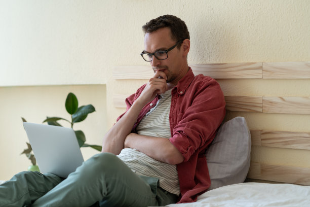 欧洲男子投资者工作，坐在卧室的床上，通过笔记本电脑跟踪股票行情图片下载