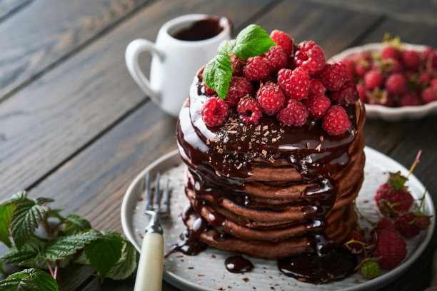 巧克力煎饼。薄煎饼与新鲜覆盆子巧克力釉或浇头在灰色的碗在旧木桌背景。自制的经典美式煎饼。页面为杂志概念。图片下载