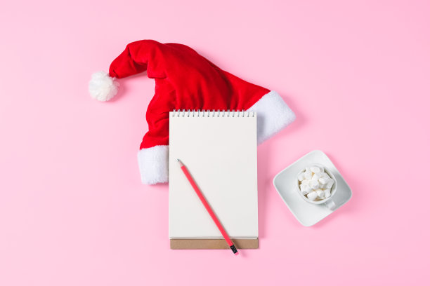 新年愿望清单概念。记事本，圣诞老人帽子和可可杯孤立在粉红色的背景。带有复制空间的节日横幅。图片下载