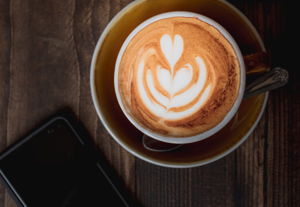 木桌上有一张心形图案的卡布奇诺，旁边是一部黑色电话图片下载