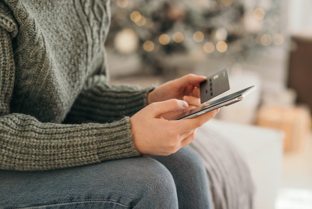 圣诞节网购，冬季打折促销，在家网购。女性手里拿着信用卡和模糊的散景灯的手机图片下载