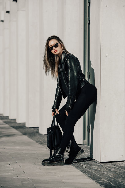 时尚的年轻女子长发，穿着结实的长袖紧身连体衣，黑色皮夹克和光滑的厚底靴图片下载