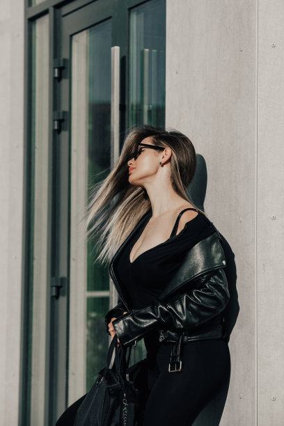时尚的年轻女子长发，穿着结实的长袖紧身连体衣，黑色皮夹克和太阳镜摆姿势图片下载