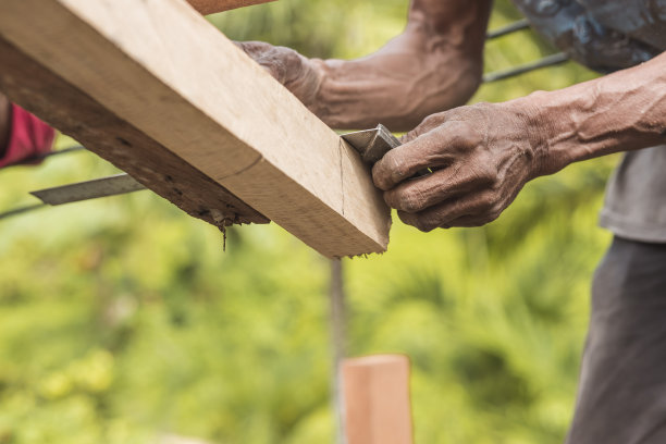 木匠用铅笔在木椽多余的边缘上做记号。用l型直尺划出一条直线。建造一个木制的屋顶框架。图片下载
