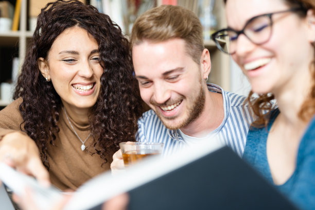 快乐的白人朋友在大学图书馆玩得很开心，坐在桌子边看书边喝咖啡和茶。图片下载