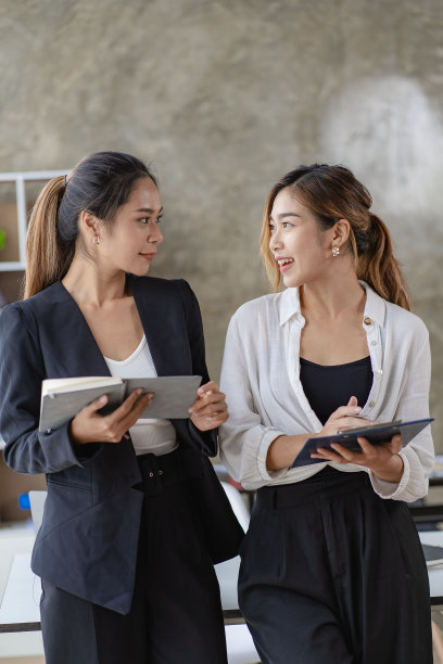 2个漂亮的亚洲女孩专业成功的商业女性模特。微笑着拿着平板电脑站在办公室里聊天图片下载