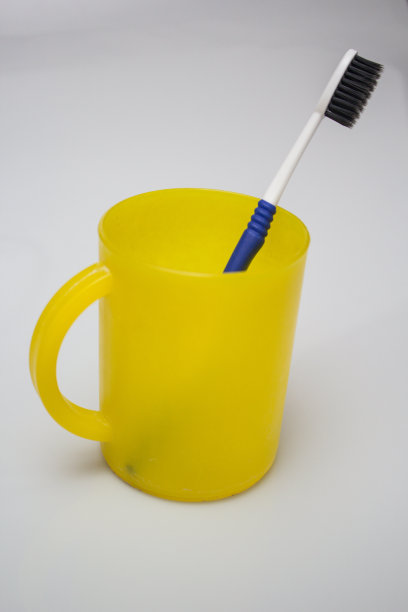 垂直拍摄的牙刷在一个黄色的塑料杯与白色的背景图片下载