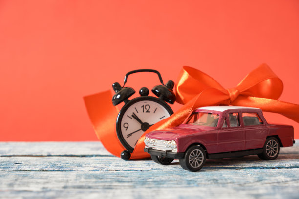 微型紫色复古汽车模型，红色丝带蝴蝶结和闹钟在木制表面，红色背景图片下载