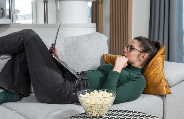 年轻的自由职业者商业女性坐在家里吃爆米花，看着她的新小互联网下降航运公司在线提高订单和收入的统计数据。成功的商人。图片下载
