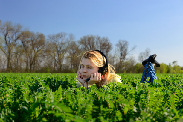 年轻女子戴着耳机在草地上听音乐图片下载