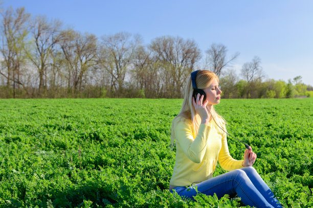 年轻女子戴着耳机在草地上听音乐图片下载
