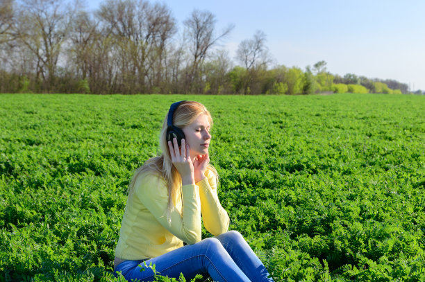 年轻女子戴着耳机在草地上听音乐图片下载