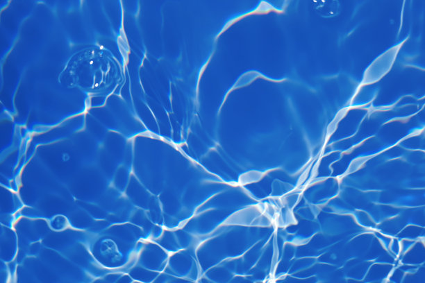 离焦模糊透明蓝色清澈平静的水面纹理与飞溅和气泡。新潮抽象的自然背景。阳光下的水波与复制空间。蓝色水彩闪亮的图片下载