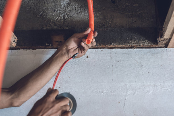 电工或杂工正在往一根橙色PVC波纹软管内插入电线图片下载