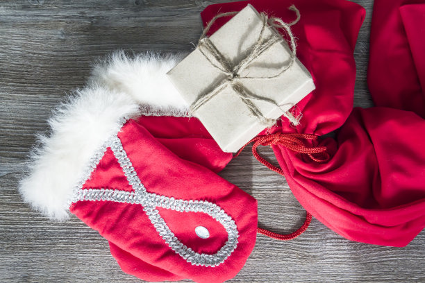 红色的圣诞老人手套和一个木制表面的工艺包装的礼物盒子。图片下载