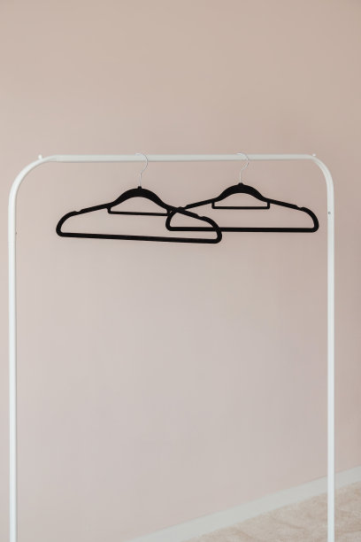 白色衣服上的黑色空衣架挂在粉红色的墙上图片下载