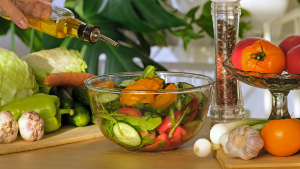橄榄油倒在蔬菜沙拉上。夏日有机沙拉碗。将橄榄油倒在新鲜的希腊蔬菜沙拉上，包括西红柿，黄瓜，辣椒，葱花，洋葱。健康食品的特写图片下载