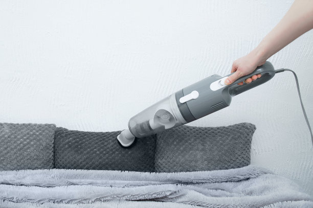 手持吸尘器在手。床上有真空吸尘器和装饰枕头。图片下载