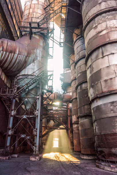 旧的令人毛骨悚然的肮脏的冒烟工厂，阳光穿透金属结构和管道图片下载