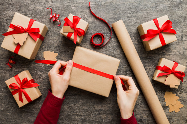 女人正在为圣诞假期打包惊喜礼物，坐在工作场所用手工工具，俯视。在彩色桌子上包装圣诞礼物的妇女图片下载
