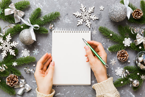 女人写圣诞做清单在笔记本上彩色背景与圣诞装饰图片下载