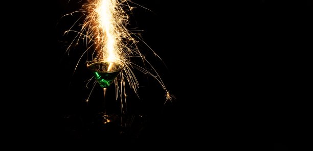 绿色鸡尾酒装在玻璃杯中，火花反射在黑色背景的玻璃杯中图片下载