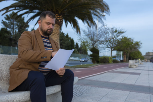 公园里一个男人坐在长凳上读文件。图片下载