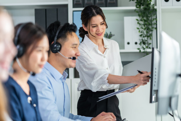 一组商务男女呼叫中心工作在办公室公司。有魅力的年轻员工坐在桌子上，戴着耳机，使用笔记本电脑在工作场所与客户交谈。图片下载