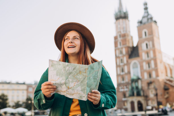 迷人的年轻女游客正在探索新的城市。在克拉科夫市场广场上，戴着帽子的红发女孩手持纸质地图。秋天去欧洲旅游。圣玛丽教堂图片下载