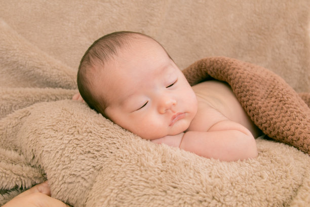 亚洲新生儿在家里安静地睡在棕色毯子里，可爱的婴儿睡在梦中。1-2个月大的幼童安全可靠地躺在床上。家人早上在家，孩子卫生。图片下载