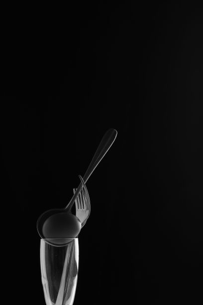 在黑色背景的玻璃杯中，竖着一把银叉和一把黑勺。图片下载