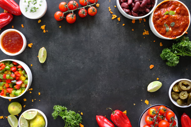 墨西哥食物设计海报框架的形象，玉米片，碗番茄莎莎，酸奶油和香葱，切片青辣椒，整个红辣椒，四豆，柠檬楔，圣女果在藤，黑色背景，墙纸背景，复制空间图片下载