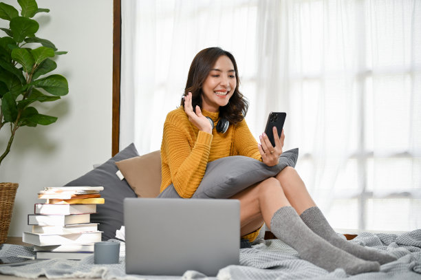 快乐的亚洲女子一边在客厅放松，一边用智能手机打电话。图片下载