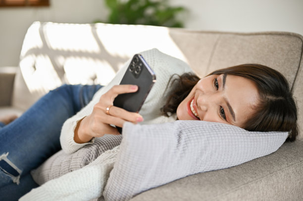 特写图片，美丽的亚洲女人躺在沙发上使用她的智能手机。图片下载