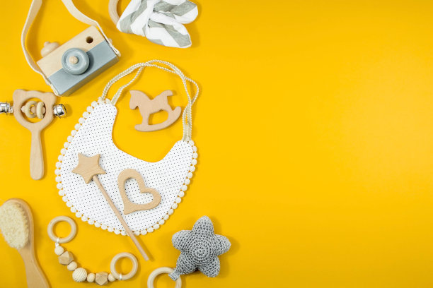 围嘴和木制玩具。一套黄色背景的女孩用的儿童用品和配件。儿童灵魂的概念。时尚的新生儿。平床，俯视图。图片下载