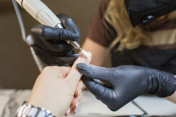 硬件修甲采用电动装置机。涂指甲油前准备指甲的程序。手戴黑色手套的美甲师和客户的指甲。美容院里的女人。图片下载