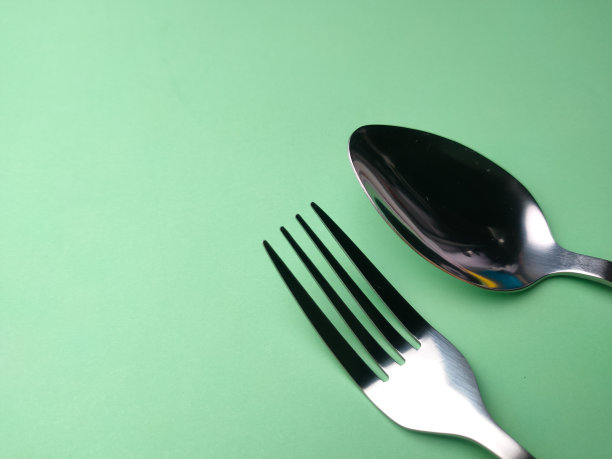 不锈钢叉子和勺子排列在绿色的背景..图片下载