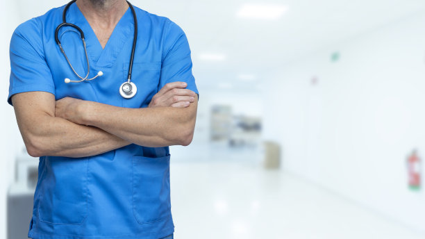 外科医生或男护士穿着蓝色工作服，双臂交叉，听诊器放在医院走廊里。保健和健康保险概念。图片下载