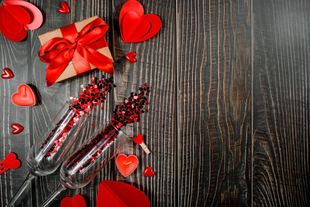 两杯五彩纸屑，红心，一个礼品盒，和蜡烛在木制背景与复制空间。这个节日的概念是所有恋人的。情人节贺卡。图片下载