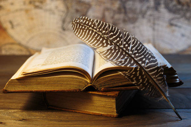 把羽毛笔放在打开的古书上。图片下载